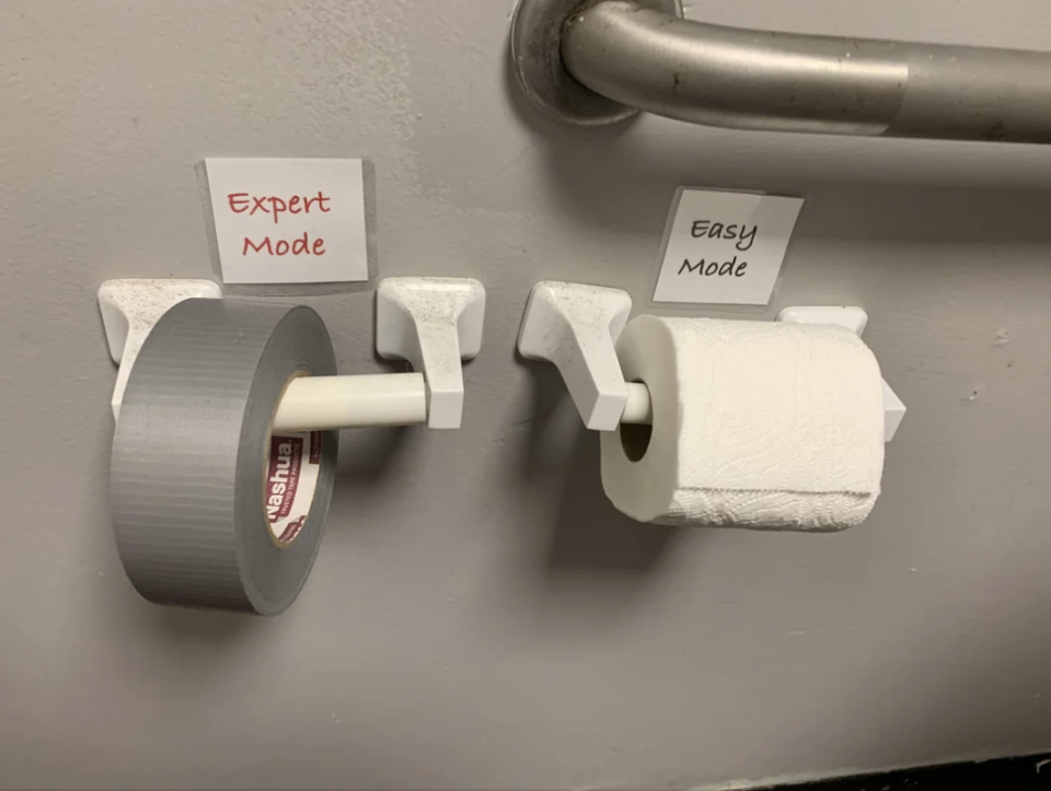 A roll of duct tape labeled "Expert Mode" is beside a roll of toilet paper labeled "Easy Mode" on a restroom wall