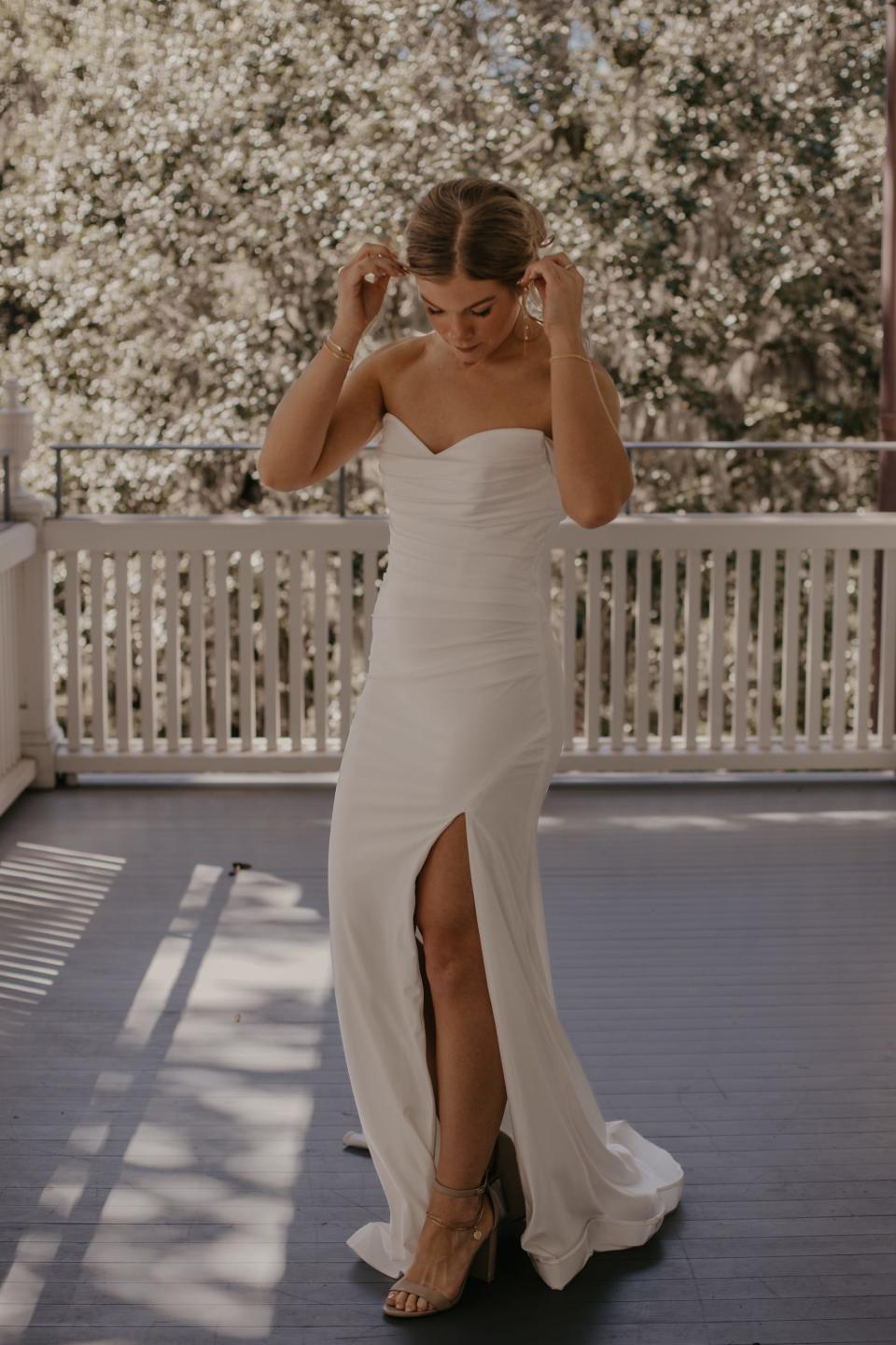 A bride looks down at her wedding dress on a porch.