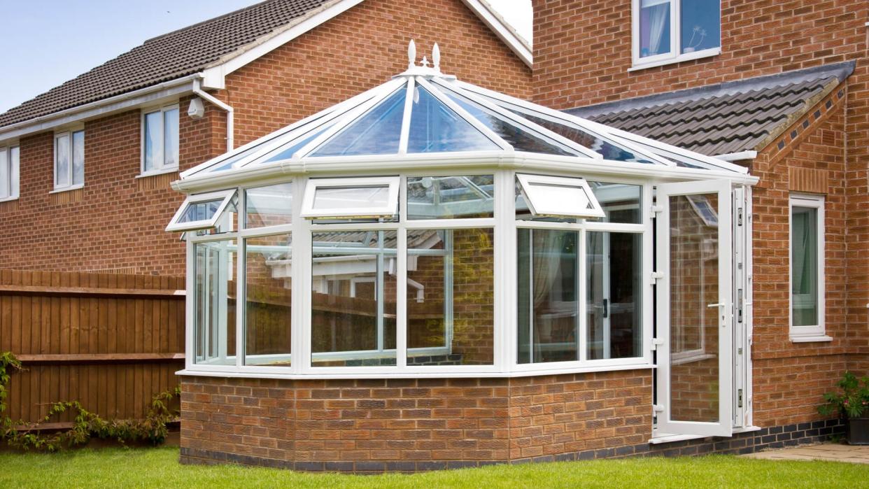 Conservatory with glass roof against a red brick house.