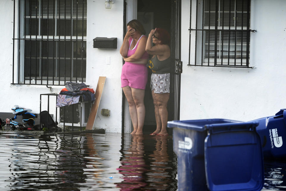 Two women react as they see flooding on their street on Thursday in North Miami, Fla.