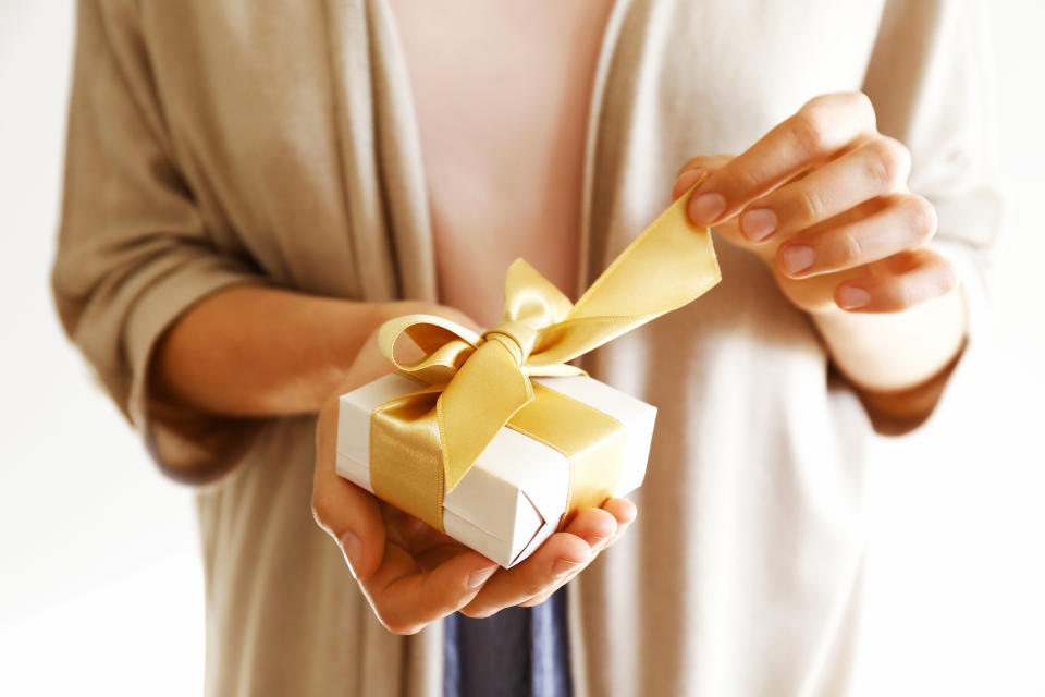 Young casual woman wearing pink shirt and long beige cardigan holding a beautiful present in shiny wrapping tied with golden bow. Unwrapping gift concept. Background, copy space, close up.