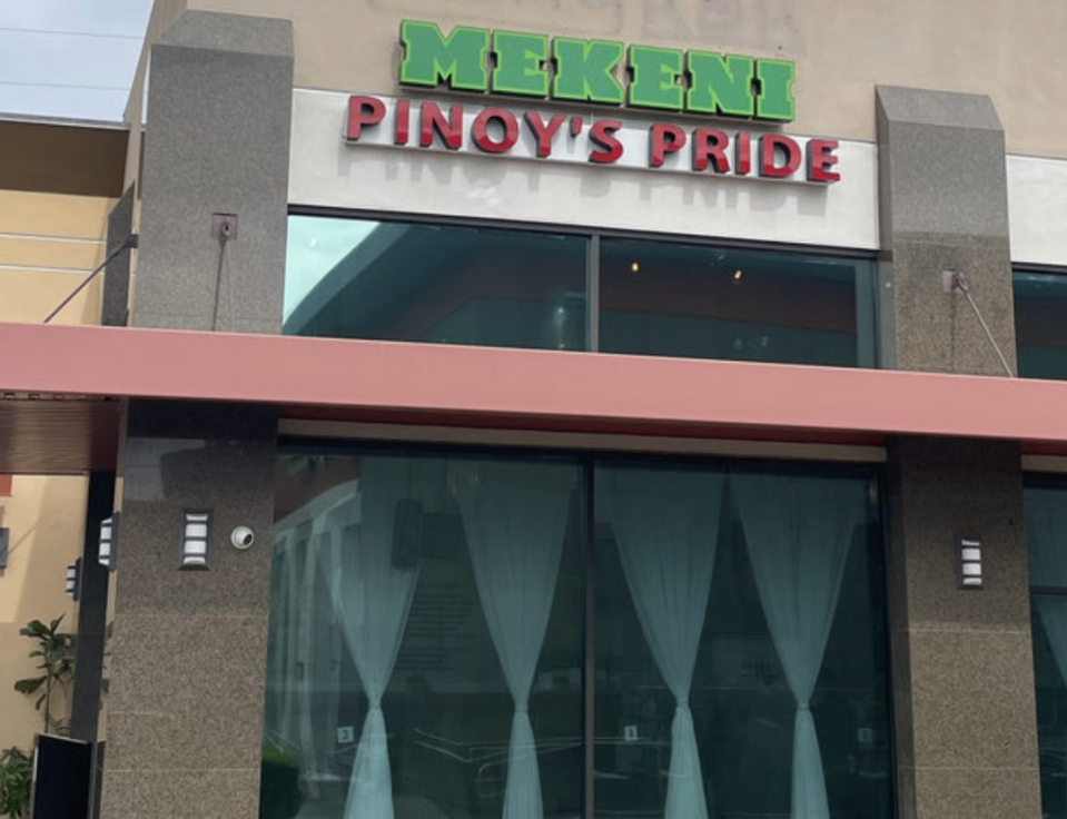 Exterior view of Mekeni Pinoy's Pride restaurant. The building has tall glass windows with curtains and a sign above the entrance
