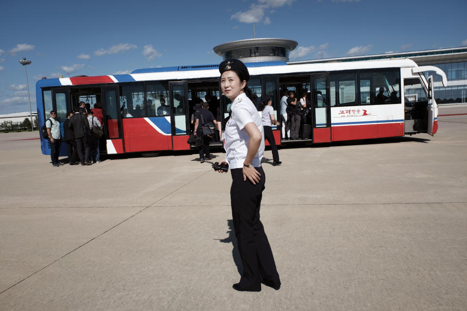 A North Korean airport worker guides passengers, including foreign journalists invited for the 70th anniversary of North Korea's founding day, onto buses after arriving on a plane at the airport in Pyongyang, North Korea, Friday, Sept. 7, 2018. North Korea will be staging a major military parade, huge rallies and reviving its iconic mass games on Sunday to mark its 70th anniversary as a nation. (AP Photo/Kin Cheung)