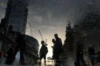 City workers are reflected in a puddle as they walk into the City of London, Britain October 16, 2017. Picture has been rotated 180 degrees. Picture taken October 16, 2017. REUTERS/Mary Turner