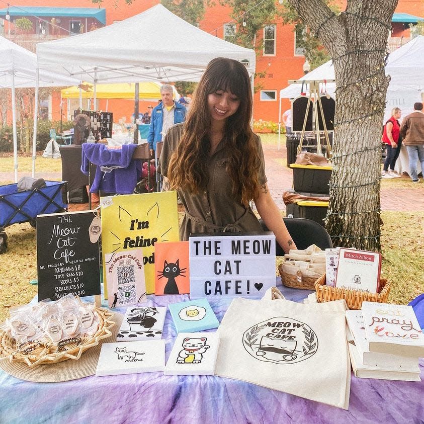 Salena Le poses with The Meow Cat Café merchandise at the Farmer's Market downtown.