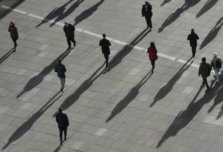 FILE PHOTO: People cast long shadows in the winter sunlight as they walk across a plaza in the Canary Wharf financial district of London