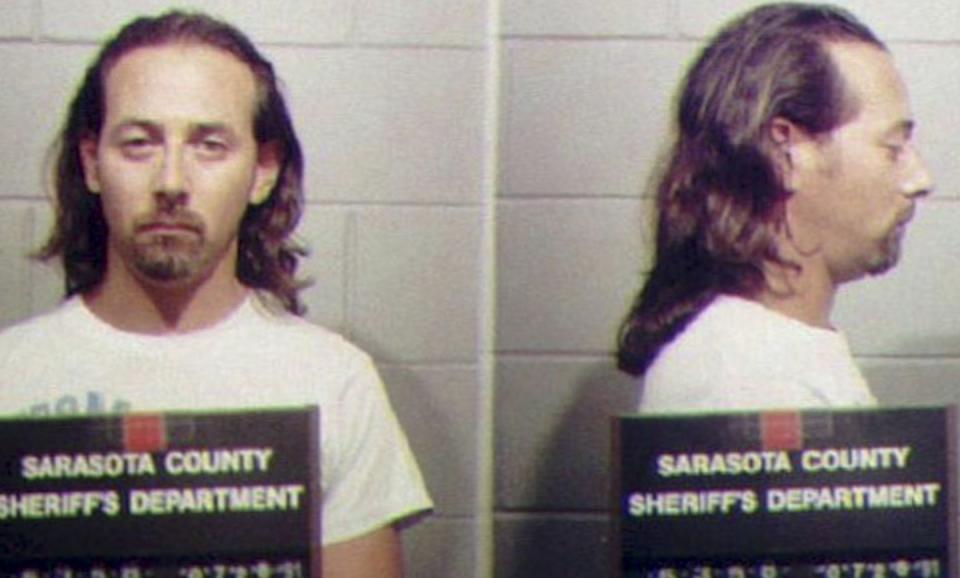 paul reubens, with long hair and a beard, posing for mugshots while holding a sarasota county sheriff's department sign
