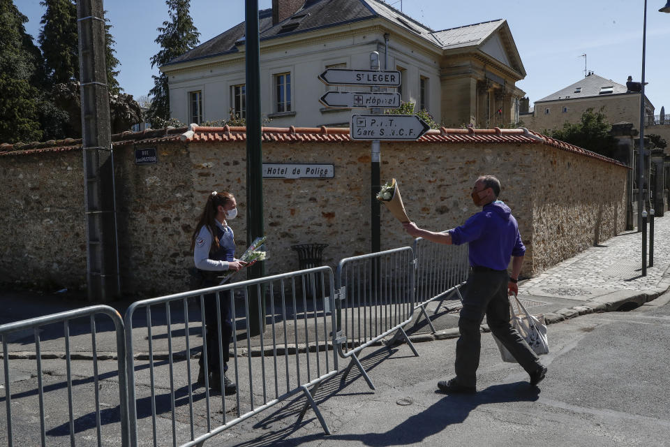 A man hands flowers to a police officer to be taken down to the police station where a police official was stabbed to death Friday in Rambouillet, south west of Paris, Saturday, April 24, 2021. Anti-terrorism Investigators were questioning three people Saturday detained after the deadly knife attack a day earlier on a police official at the entry to her station in the quiet town of Rambouillet, seeking a motive, purported ties to a terrorist group and whether the attacker, killed by police, acted alone. (AP Photo/Michel Euler)