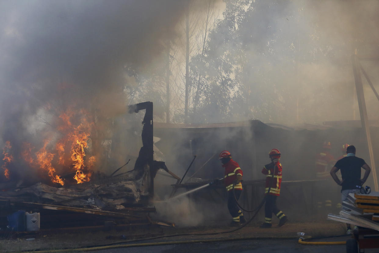 Firefighters work to control a fire next to warehouses in Sever do Vouga, a town in northern Portugal that has been surrounded by wildfires fires, Monday, Sept. 16, 2024. (AP Photo/Bruno Fonseca)