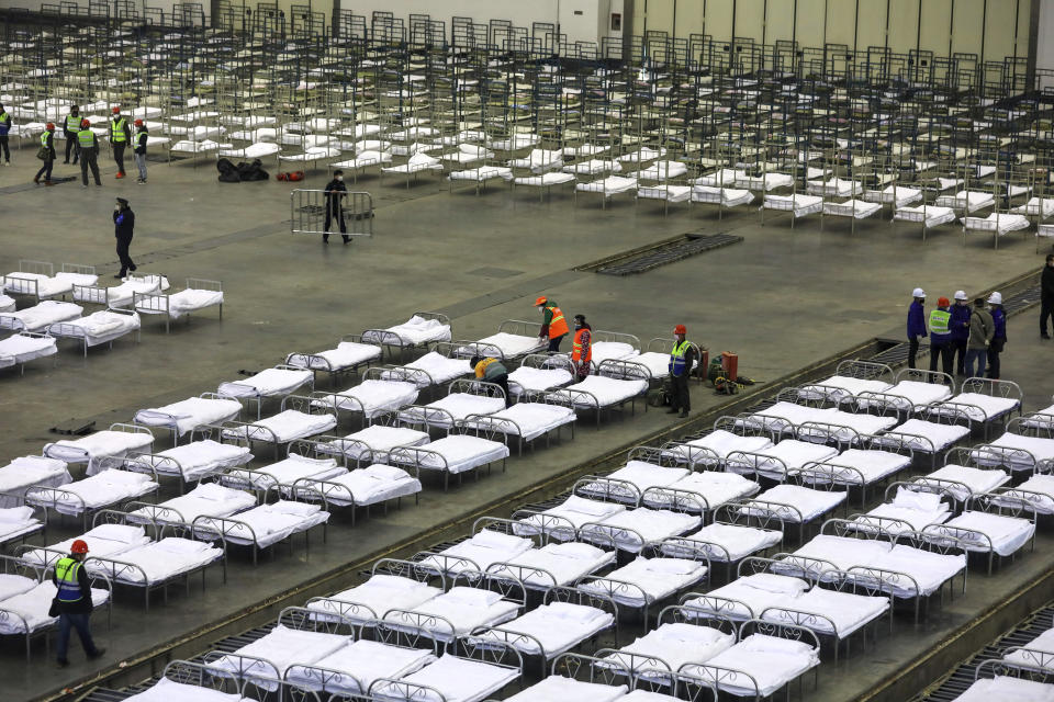 Workers arrange beds in a convention center that has been converted into a temporary hospital in Wuhan in central China's Hubei Province, Tuesday, Feb. 4, 2020. China said Tuesday the number of infections from a new virus surpassed 20,000 as medical workers and patients arrived at a new hospital and President Xi Jinping said "we have launched a people's war of prevention of the epidemic." (Chinatopix via AP)