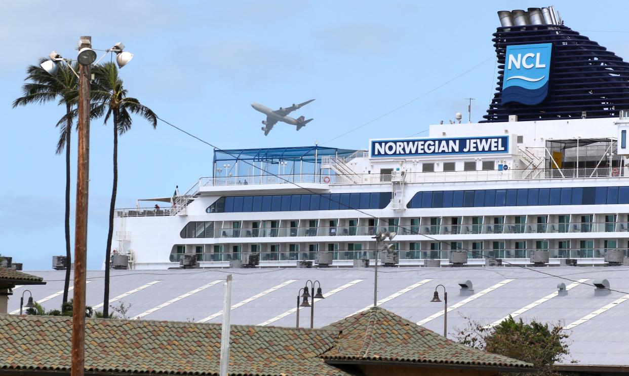 A plane takes off over the Norwegian Jewel cruise ship as it sits docked in Honolulu on Monday, March 23, 2020. Passengers from the cruise ship that was turned away from other ports before arriving in Hawaii are being taken to Honolulu airport for chartered flights home. About 2,000 passengers on the Norwegian Jewel are undergoing medical screening before boarding buses that will take them to their flights. There are no confirmed cases of coronavirus from anyone on the ship. State officials changed their minds several times before deciding over the weekend that the passengers could disembark at Honolulu Harbor. Measures to seal off borders to reduce the spread of coronavirus have left some cruise ships stranded.