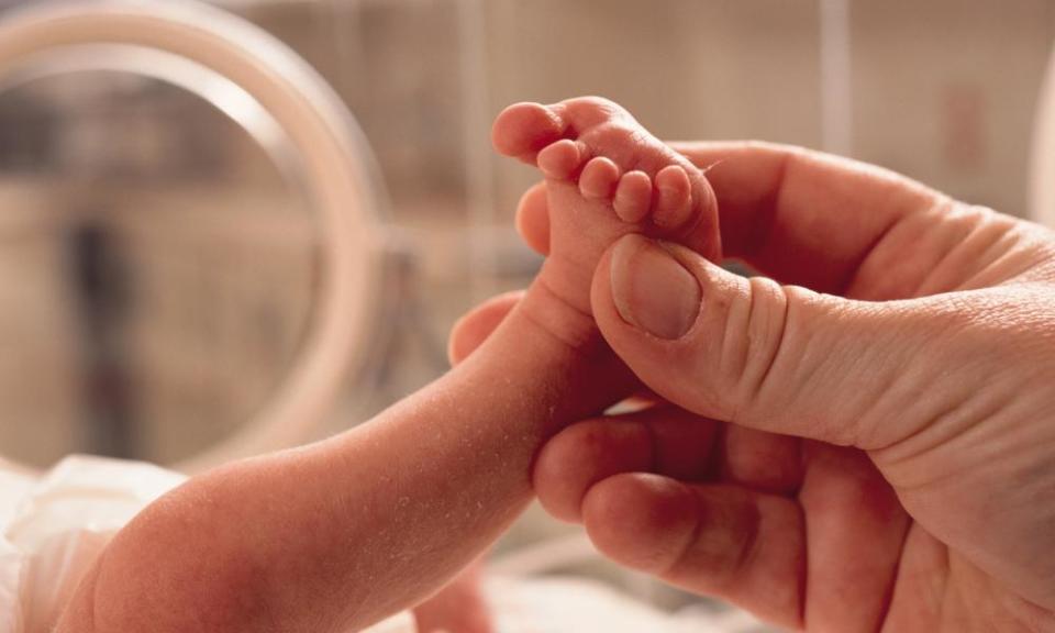 Very small premature baby’s foot held in a hand