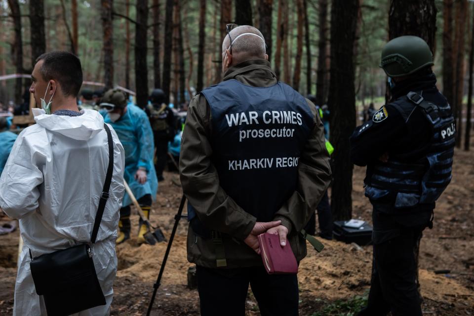 War crime prosecutor of Kharkiv Oblast stands with forensic technician and policeman at the site of a mass burial in a forest during exhumation on September 16, 2022 in Izium, Ukraine.
