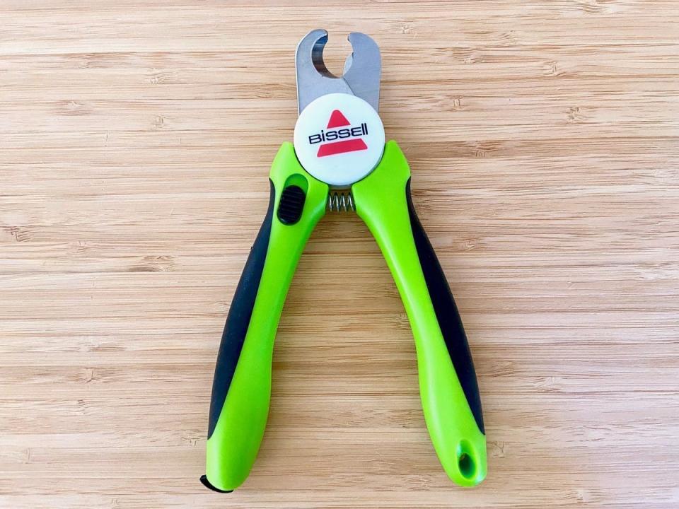 The Bissell Dog and Cat Nail Clippers with green and black handle and steel blades are on a wooden surface.