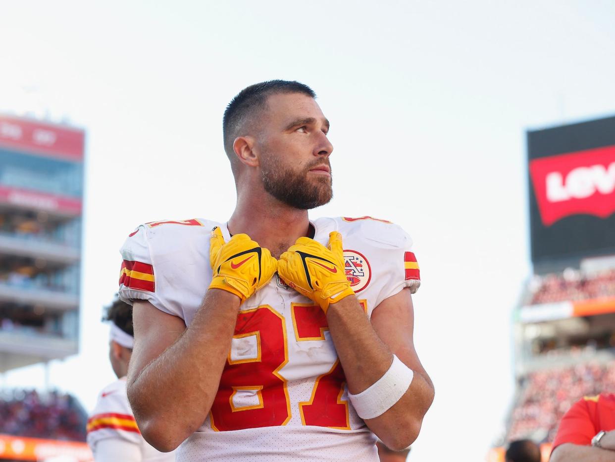 Travis Kelce rests his hands on his collar while looking off to the side during a Chiefs game.