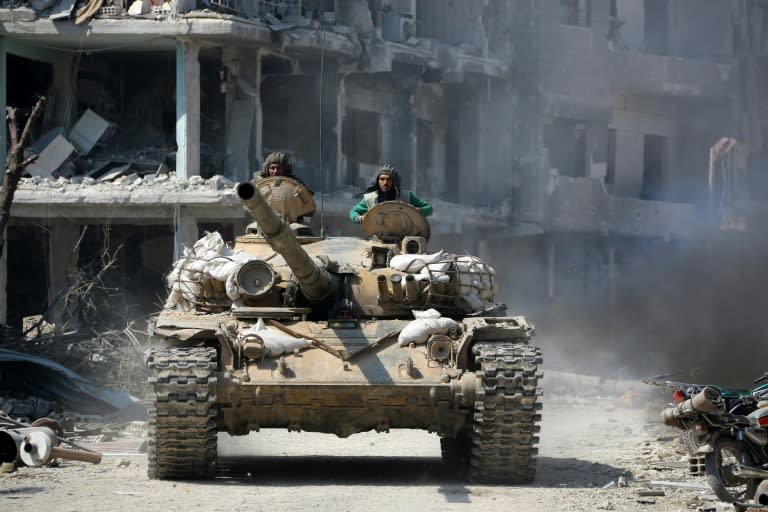 Members of the Syrian government forces ride in a tank in Eastern Ghouta on March 17, 2018