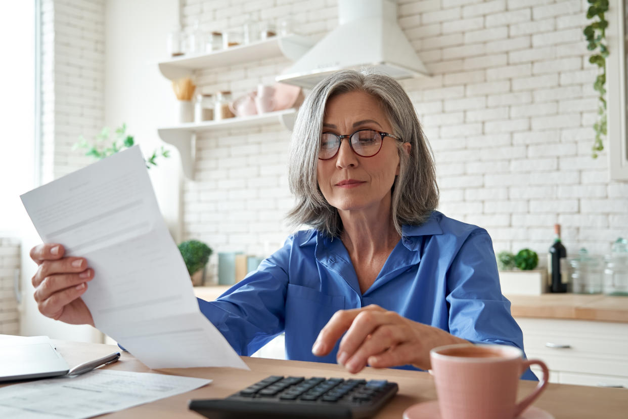 A woman with a bill and a calculator in her kitchen