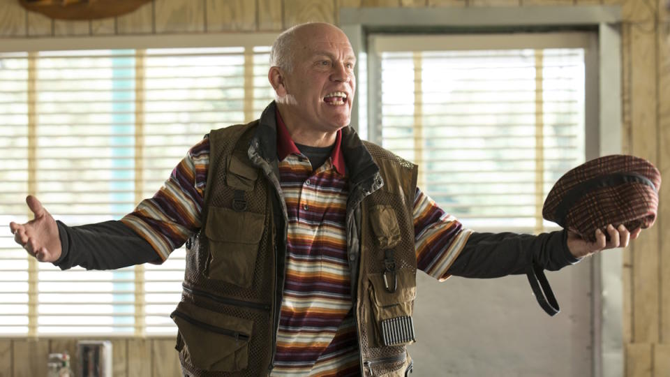 John Malkovich stands with his arms wide wearing a vest in Red 2