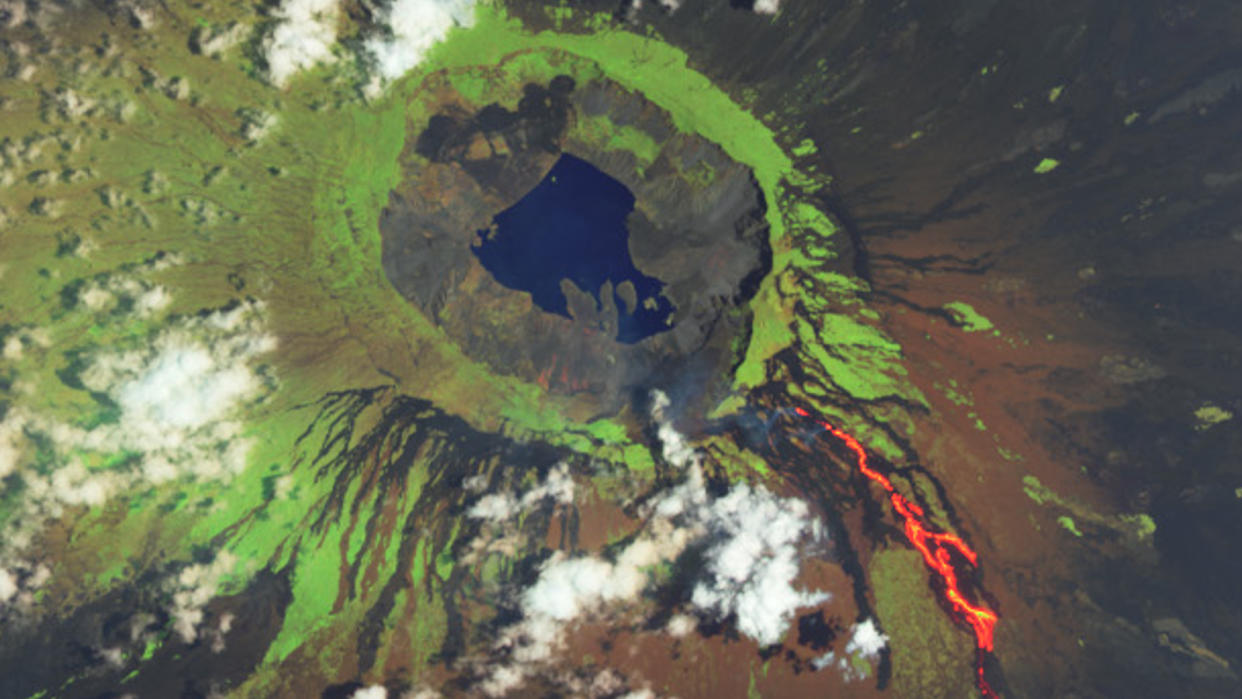  A satellite photo of a volcano with a crater lake and lava bleeeding down the side of its tree-covered slopes. 