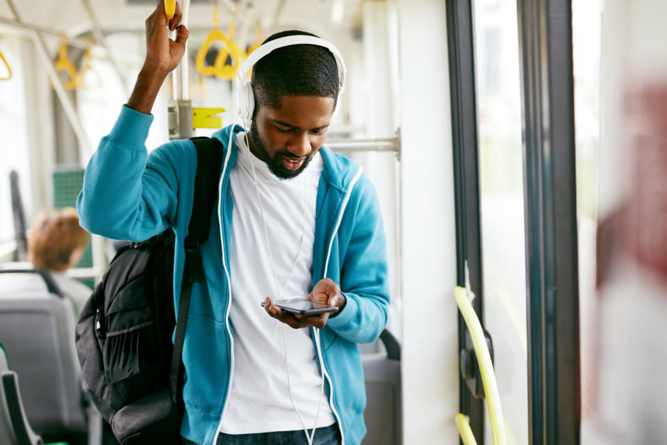 Man Using Phone, Listening Music Traveling In Train. Black Male Student With Headphones Riding In Public Transport. High Resolution