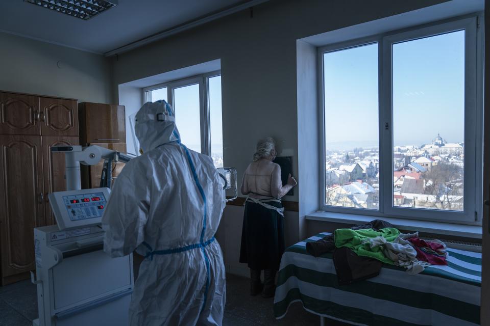 A medic wearing a special suit to protect against coronavirus, back to a camera prepares a patient with coronavirus for a lung X-ray at a hospital in Kolomyia, western Ukraine, Tuesday, Feb. 23, 2021. After several delays, Ukraine finally received 500,000 doses of the AstraZeneca vaccine marketed under the name CoviShield, the first shipment of Covid-19 vaccine doses. The country of 40 million is one of the last in the region to begin inoculating its population. (AP Photo/Evgeniy Maloletka)