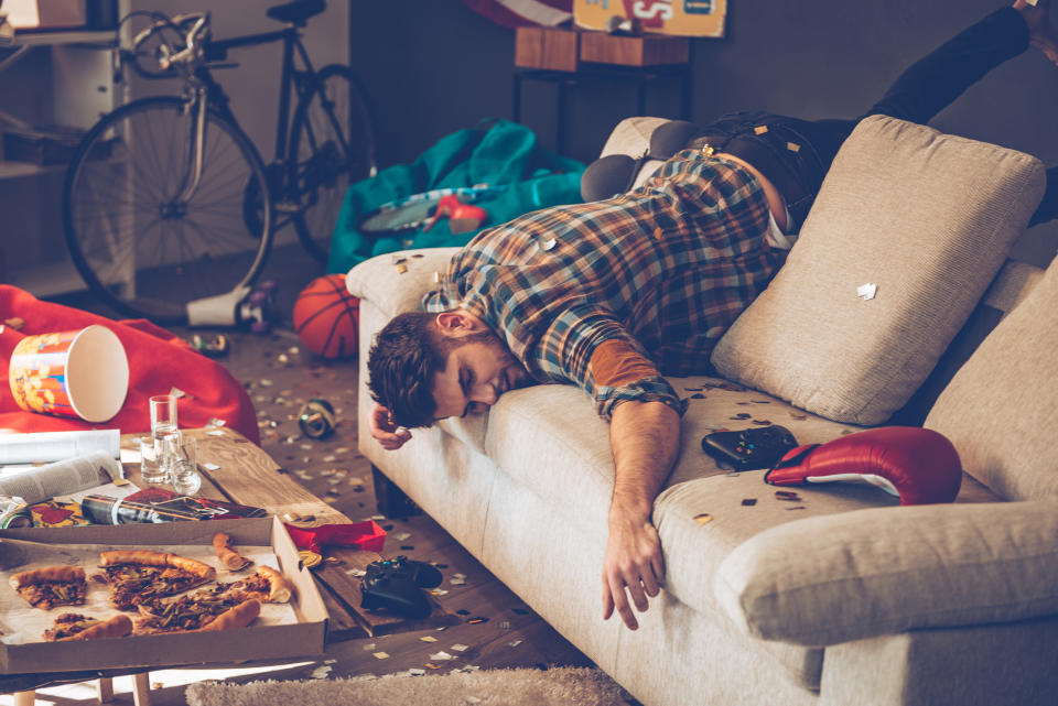 very messy room with food and trash everywhere and a person laying across the couch