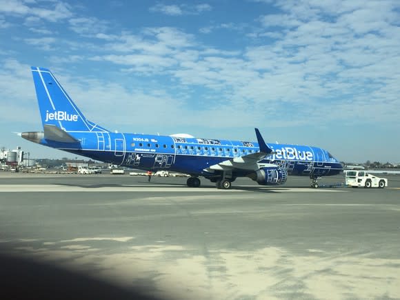 A JetBlue E190 being pulled by a tug vehicle