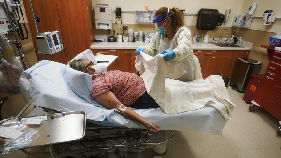 Angie Cleary, a registered nurse, cares for Joyce Johnson-Albert as she receives an antibody infusion while lying on a bed in a trauma room at the Upper Tanana Health Center Wednesday, Sept. 22, 2021, in Tok, Alaska. Johnson-Albert was optimistic but also realistic. "I just hope the next few days I'll be getting a little better than now," Johnson-Albert told a reporter on the other side of a closed, sliding glass door to the treatment room two days after testing positive for COVID-19 and while receiving an antibody infusion. "It's just hard to say. You can go either way." (AP Photo/Rick Bowmer)