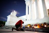 A man kneels as he brings a megaphone to a vigil on the steps of the U.S. Supreme Court following the death of U.S. Supreme Court Justice Ruth Bader Ginsburg, in Washington