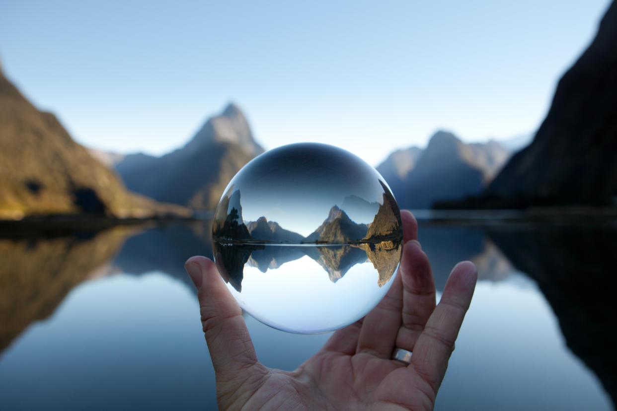 Crystal ball held by mal hand with Mitre Peak reflecting in Milford Sound