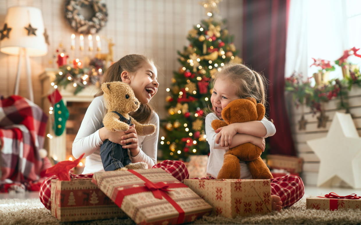 Merry Christmas and Happy Holidays! Cheerful cute childrens girls opening gifts. Kids wearing pajamas having fun near tree in the morning. Loving family with presents in room.