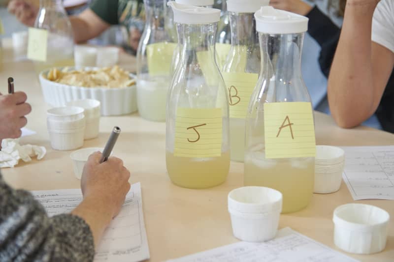 candid photo of Apartment Therapy/The Kitchn staff taste testing multiple different margarita mix flavors from pitchers and jotting down their opinions