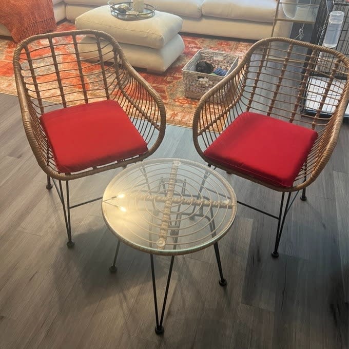 Two wicker chairs with red cushions and a small round glass table, indoors