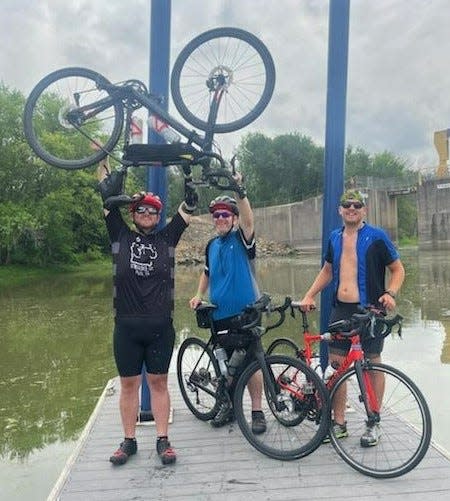 Aaron Conley, left, raises his bike after completing RAGBRAI XLVIII in Clinton on July 31, 2021. Conley and his brother Dennis, right, rode RAGBRAI with their uncle Dan Hunt, center, after losing 215 pounds each.