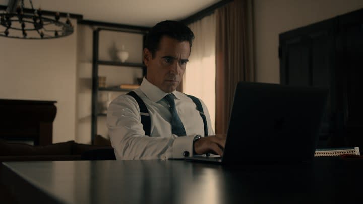 Colin Farrell as John Sugar sitting at a computer in a white shirt, tie, and suspenders in Sugar on Apple TV+.