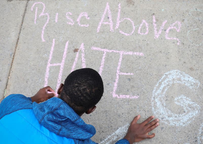 A boy writes a message on the sidewalk near a memorial in the wake of a weekend shooting at a Tops supermarket in Buffalo, New York