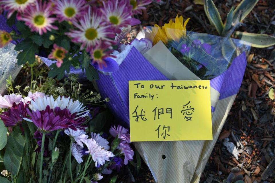 A closeup shot of a bouquet of flowers, one of many left outside a church. A note on one bouquet reads ‘To our Taiwanese family’.