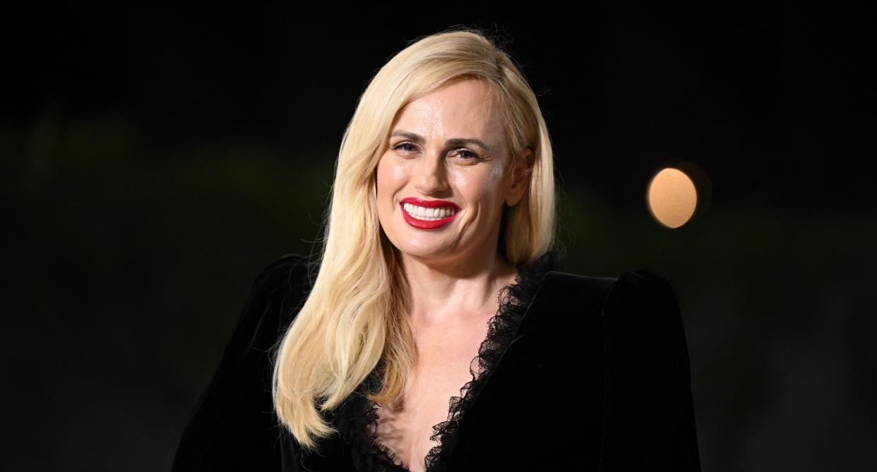 Rebel Wilson stands in front of a black background and smiles towards the camera. (Getty Images)