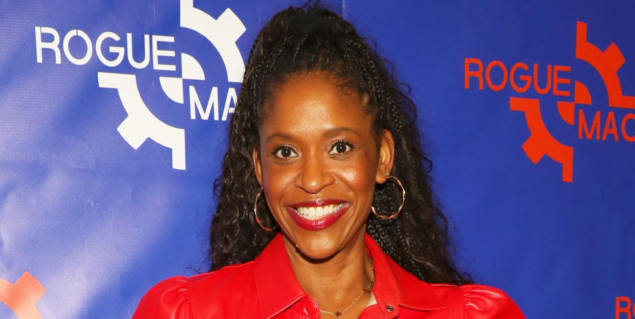 merrin dungey smiles for the camera in a red leather shirt dress and gold hopped earrings