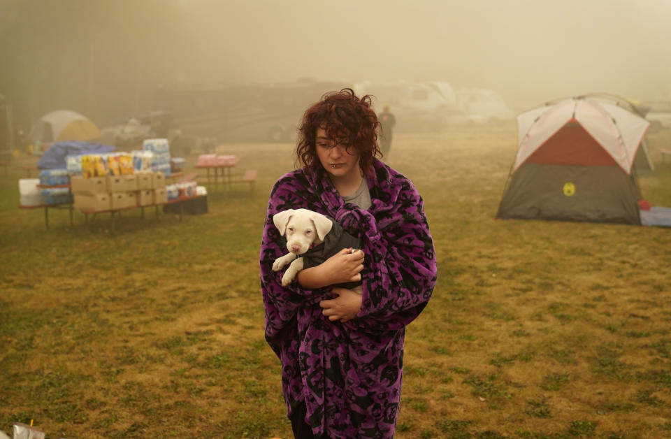 FILE - In this Sept. 13, 2020, file photo, Shayanne Summers holds her dog Toph while wrapped in a blanket after several days of staying in a tent at an evacuation center at the Milwaukie-Portland Elks Lodge in Oak Grove, Ore. "It's nice enough here you could almost think of this as camping and forget everything else, almost," said Summers about staying at the center after evacuating from near Molalla, Oregon which was threatened by the Riverside Fire. (AP Photo/John Locher, File)