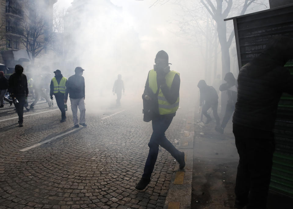 Protesters walk through tear gas during a yellow vests demonstration Saturday, March 16, 2019 in Paris. French yellow vest protesters clashed Saturday with riot police near the Arc de Triomphe as they kicked off their 18th straight weekend of demonstrations against President Emmanuel Macron. (AP Photo/Christophe Ena)