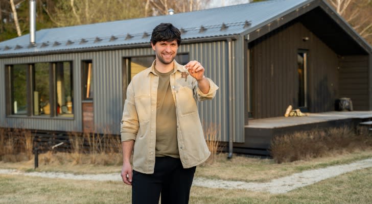 A homebuyer posing in front of a house after closing a deal.