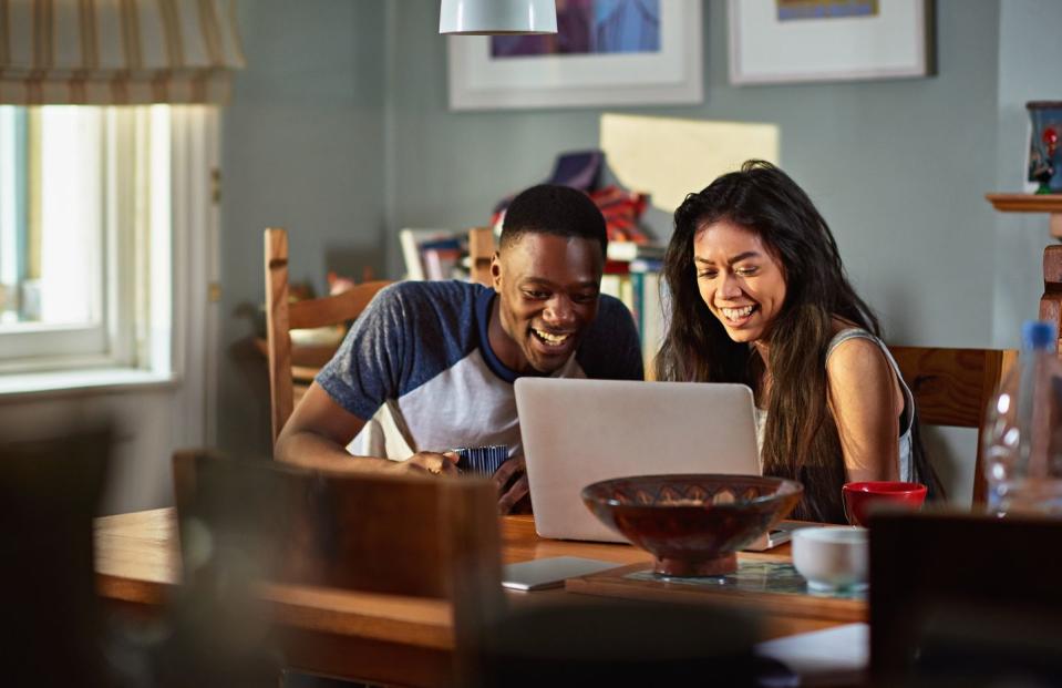 couple laughing at footage on laptop at breakfast