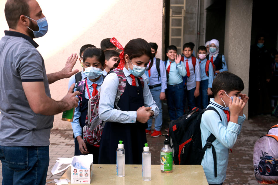 A teacher sanitizes students' hands on the playground, at a school in Baghdad, Iraq, Monday, Nov. 1, 2021. Across Iraq, students returned to classrooms Monday for the first time in a year and a half – a stoppage caused by the coronavirus pandemic - amid overcrowding and confusion about COVID-19 safety measures. (AP Photo/Hadi Mizban)