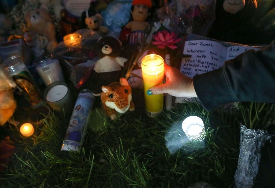 A mourner places a candle on a growing memorial as family, friends, classmates and community members gather Friday, May 10, 2024 where James Raul Messick, 10, was struck on his walk home from school by a vehicle that left the roadway. The gathering followed a vigil at nearby Marbrook Elementary School where the boy was a student.