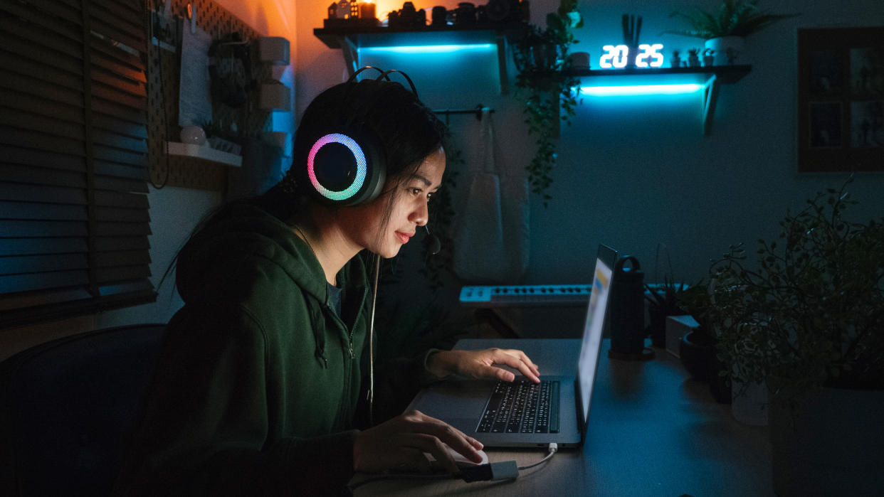  Gamer with headphones and laptop in dark room. 