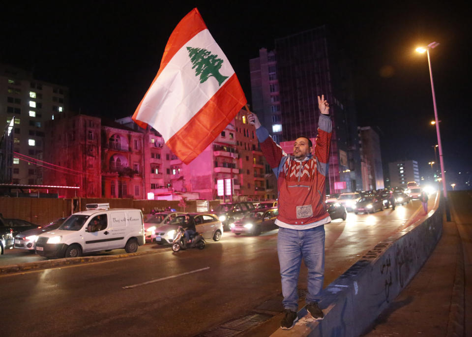 An anti-government protester flashes the victory sign and waves a Lebanese flag, as other protesters block a main road during ongoing protests against the ruling elite of corruption and financial crisis, in Beirut, Lebanon, Monday, Jan. 13, 2020. Lebanon is facing its worst economic crisis in decades, while protests against corruption and mismanagement have gripped the country since October. (AP Photo/Hussein Malla)