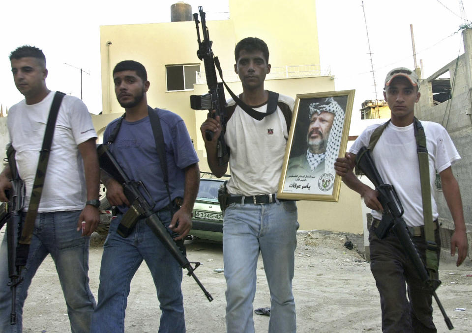 FILE - In this July 31, 200 file photo, Palestinian Zakaria Zubeidi, then leader of the Al-Aqsa Martyrs' Brigades militant group in the West Bank town of Jenin, holds a picture of Yasser Arafat, as he poses with other militants after they set the town's Governorate on fire overnight. For nearly two decades, Zubeidi has been an object of fascination for Israelis and Palestinians alike, who have seen his progression from a child actor to a swaggering militant, to the scarred face of a West Bank theater promoting “cultural resistance” to Israeli occupation. In his latest act, he has emerged as one of Israel's most wanted fugitives after tunneling out of a high-security prison on Monday, Sept. 6, 2021 with five other Palestinian militants. (AP Photo/Mohammed Ballas, File)