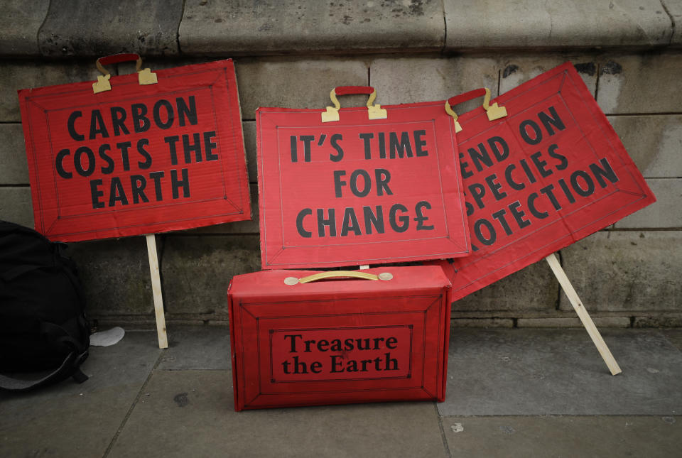 A facsimile of the budget box with a message 'treasure the earth' sits among other protest signs prior to a demonstration on the budget outside Parliament in London, Wednesday, March 11, 2020. Britain's Chancellor of the Exchequer Rishi Sunak will announce the first budget since Britain left the European Union. (AP Photo/Matt Dunham)