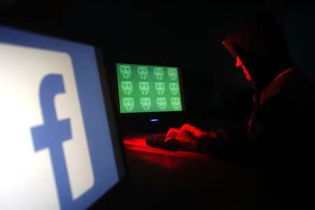 Man poses in front of on a display showing a Facebook logo and the word 'cyber' in binary code, in this picture illustration taken in Zenica December 27, 2014. REUTERS/Dado Ruvic/Files